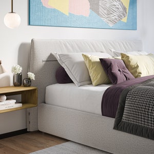 K&ouml;nnte beinhalten: Ein wei&szlig;es Bett mit einem grauen Kopfteil und einer grau-schwarzen gemusterten Decke. Das Bett hat einen schwebenden Nachttisch aus Holz mit zwei B&uuml;chern und einer Vase mit wei&szlig;en Blumen darauf. Auf dem Nachttisch steht eine Lampe und &uuml;ber dem Bett h&auml;ngt eine wei&szlig;e Kugel-Pendelleuchte.
