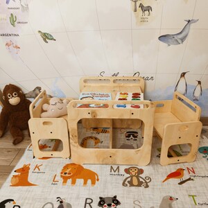 Puede incluir: Un juego de mesa y sillas de madera para ni&ntilde;os con un libro titulado "Sen &Ccedil;ikolatalı Kurabiye" en la mesa. El juego est&aacute; sobre una alfombra de juego de alfabeto gris y blanco.