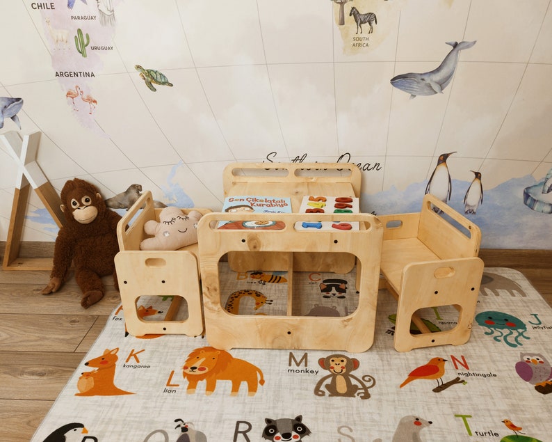 Puede incluir: Un juego de mesa y sillas de madera para ni&ntilde;os con un libro titulado "Sen &Ccedil;ikolatalı Kurabiye" en la mesa. El juego est&aacute; sobre una alfombra de juego de alfabeto gris y blanco.