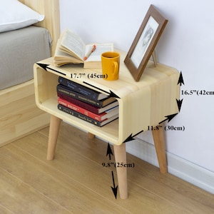 May include: A light wood bedside table with a curved shelf and four legs. The table is 17.7 inches wide, 16.5 inches tall, and 11.8 inches deep. The legs are 9.8 inches tall.