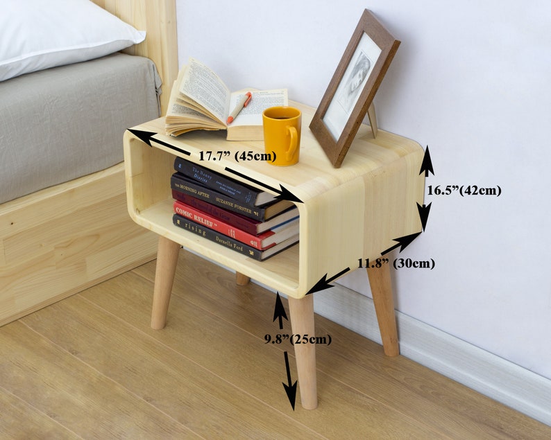 May include: A light wood bedside table with a curved shelf and four legs. The table is 17.7 inches wide, 16.5 inches tall, and 11.8 inches deep. The legs are 9.8 inches tall.