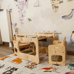 Puede incluir: Una mesa de juego de madera para ni&ntilde;os y dos sillas, colocadas sobre una alfombra con ilustraciones de animales. La mesa tiene un acabado de madera clara y un peque&ntilde;o estante debajo. Las sillas tambi&eacute;n est&aacute;n hechas de madera clara y tienen un dise&ntilde;o sencillo.