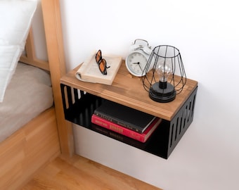 May include: A black metal wall shelf with a wooden top. The shelf has a wire cage lamp with a light bulb and a white alarm clock on the top shelf. There are books and sunglasses on the top shelf.