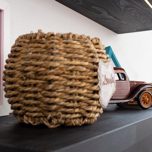K&ouml;nnte beinhalten: Ein geflochtener Korb mit einem Etikett mit der Aufschrift "Sweet" neben einem Holzspielzeug-LKW mit orangefarbenen R&auml;dern. Der Korb besteht aus einem hellbraunen Material und ist rund. Der LKW ist braun und hat ein detailliertes Design.