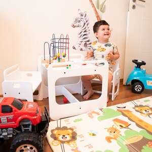 May include: A white wooden play table and chairs set with a colorful bead maze toy. A child sits at the table, and a red toy truck and a blue toy car are on the floor. A colorful play mat with animal designs is on the floor.