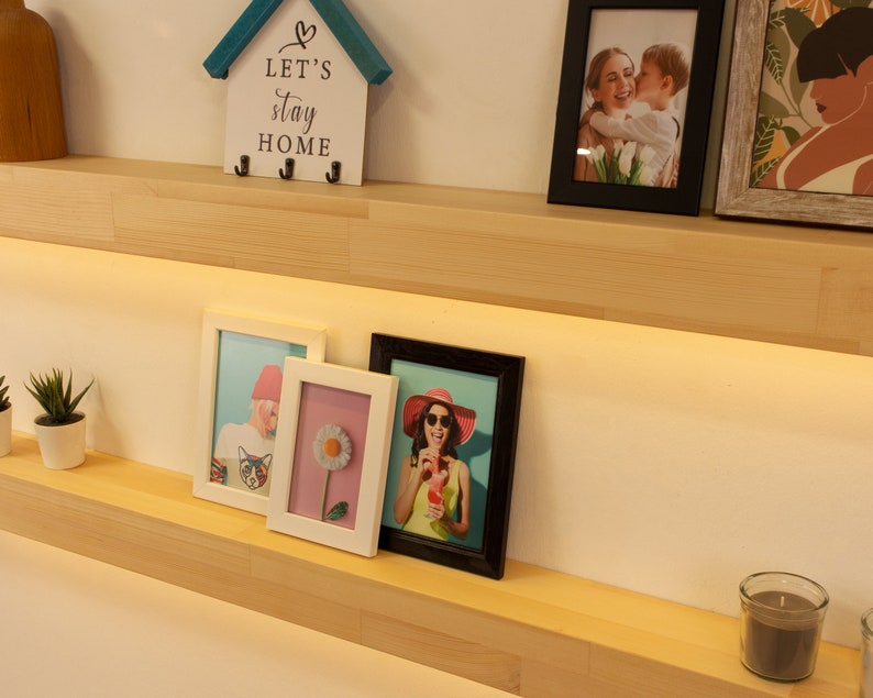 May include: A display of framed photos and decorative items on a wooden shelf. The frames are black and white, holding various images. A small house-shaped key holder with the text "LET'S stay HOME" is also present.