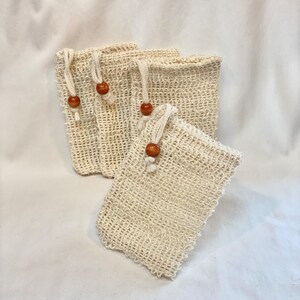 May include: Four natural beige exfoliating bath poufs with wooden toggles. The poufs are made of a woven mesh material.