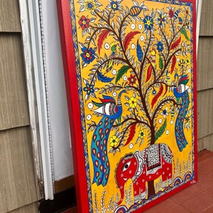 Puede incluir: Una pintura colorida sobre lienzo que representa un &aacute;rbol con pavos reales y un elefante. El &aacute;rbol est&aacute; lleno de flores y p&aacute;jaros. El fondo es amarillo y el marco es rojo.