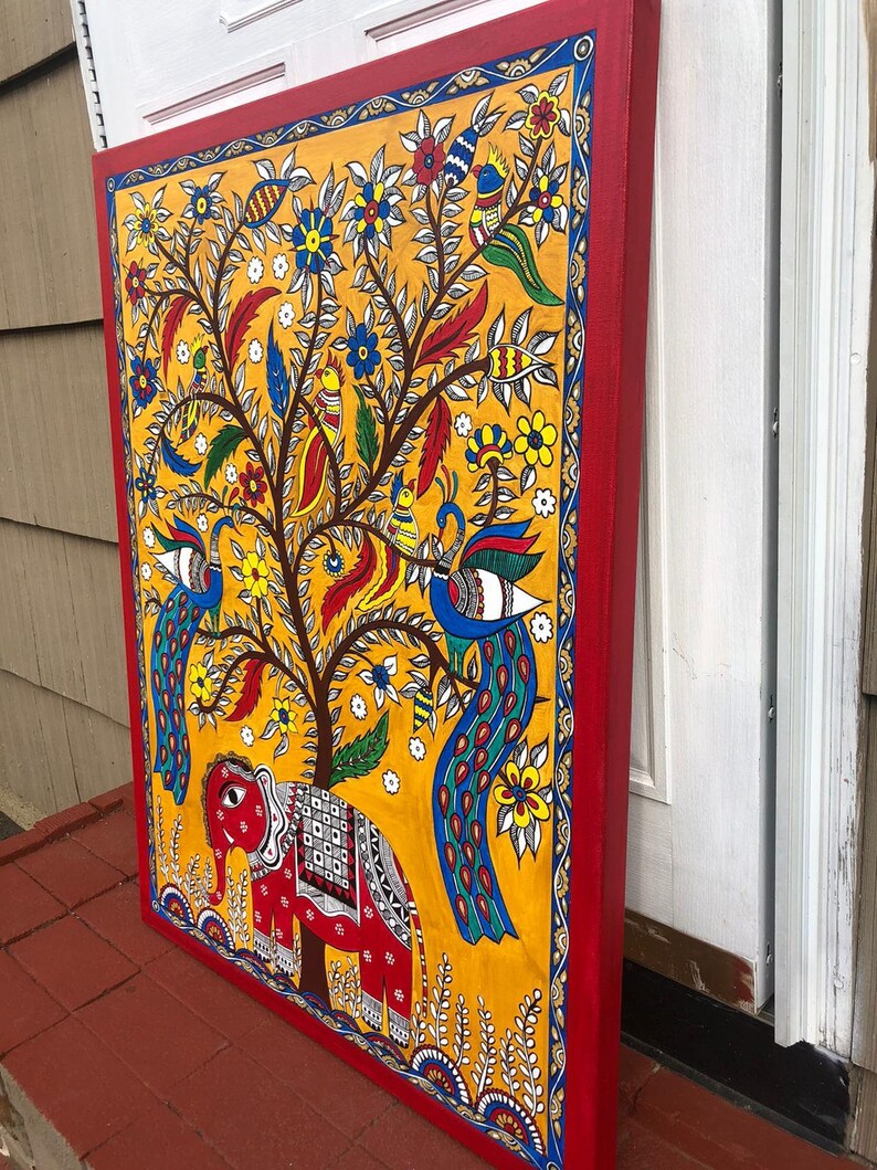 Puede incluir: Una pintura colorida sobre lienzo que representa un &aacute;rbol con pavos reales, p&aacute;jaros y un elefante. El &aacute;rbol est&aacute; pintado en tonos de amarillo, verde y marr&oacute;n, con flores en rojo, azul y blanco. Los pavos reales son azules y verdes con colas largas. El elefante es rojo con detalles blancos. La pintura est&aacute; enmarcada en un borde rojo.
