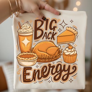 May include: A cream-colored tote bag featuring a Thanksgiving-themed graphic. The design includes a turkey, pie, cupcake, and a beverage, with the words "Big Back Energy" in a decorative font. The illustrations are in shades of orange and brown.