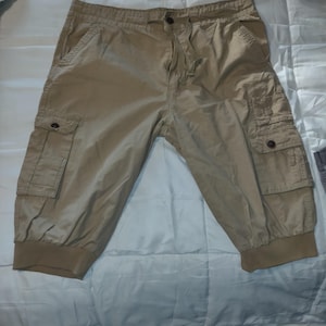 May include: Khaki-colored cargo shorts with multiple pockets and a drawstring waist. The shorts have a relaxed fit and are made of a lightweight fabric. The shorts have a button closure and elastic cuffs at the bottom of the legs.