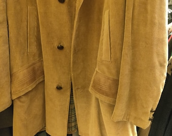 May include: A long, tan corduroy jacket with a button-up front and two pockets on the front. The jacket has a suede-like trim on the pockets and sleeves.