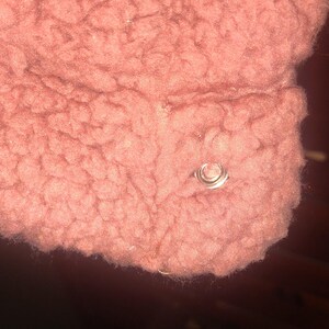 May include: Close-up of a section of a dusty rose-colored, textured fabric. A silver-colored, circular metal snap is visible on the fabric. The fabric appears to be a soft, fuzzy material.