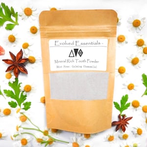 May include: A tan pouch containing mineral rich tooth powder with a label reading Evolved Essentials, Mineral Rich Tooth Powder, Mint Free: Calming Chamomile. The pouch features a clear window showing the light grey powder inside the packaging.