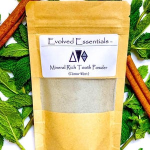 May include: A tan paper pouch of Evolved Essentials Mineral Rich Tooth Powder in Cinna-Mint flavour. The label features a geometric logo and text. The pouch has a clear window showing the light-coloured powder inside, surrounded by fresh green mint leaves and brown cinnamon sticks.
