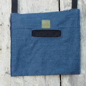 May include: A denim blue crossbody bag with a black mesh pocket and a small green patch. The bag has a black strap and is made of a sturdy fabric. The bag is designed to be worn across the body.