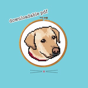 May include: A cross-stitch pattern of a yellow Labrador Retriever dog's head in a wooden embroidery hoop. The pattern is available as a downloadable PDF.