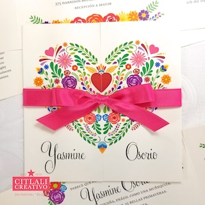 May include: A white wedding invitation with a pink ribbon tied in a bow. The invitation features a colorful heart design with flowers and leaves. The text "Yasmine Osorio" is printed in black at the bottom of the invitation.