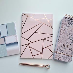 May include: Stationery set featuring a pink geometric notebook, a floral "TO DO" list notepad, and pastel-colored sticky notes. A rose gold pen with a diamond-shaped top is also included in the image.
