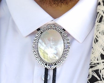 May include: A silver bolo tie with a white mother-of-pearl oval stone in the center. The tie is on a white shirt with a black and white patterned scarf.