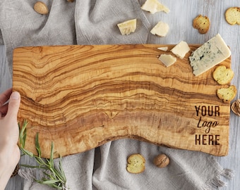 May include: A large, natural wood cutting board with a wavy edge. The board has a light brown color with dark brown grain patterns. The text "YOUR LOGO HERE" is engraved on the board.