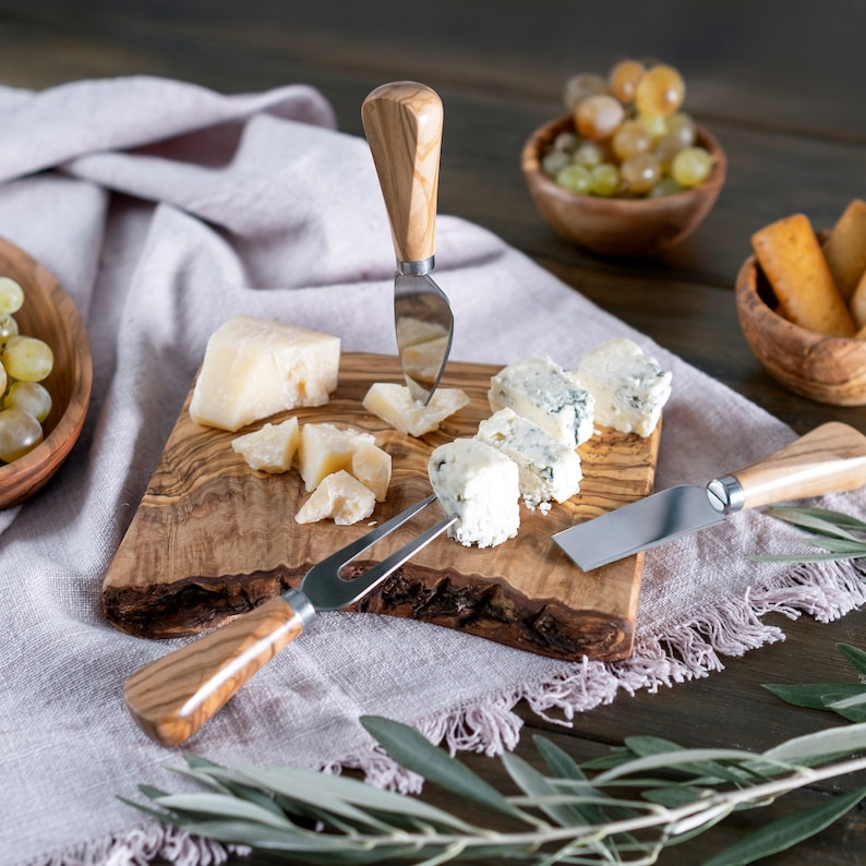 May include: A wooden cheese board with a variety of cheeses, including blue cheese, parmesan, and a fork and knife.