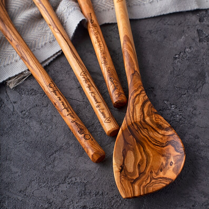 May include: Four wooden spoons with engraved sayings. The sayings are "You're my secret ingredient", "All You Knead is Love", and "You're no recipe for success".