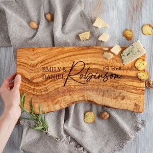 May include: Personalized olive wood cutting board with the text "Emily & Daniel Robinson Est. 2018" engraved on the surface.