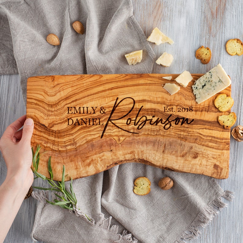 May include: Personalized olive wood cutting board with the text "Emily & Daniel Robinson Est. 2018" engraved on the surface.