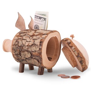 K&ouml;nnte beinhalten: Ein h&ouml;lzernes Sparschwein in Form eines Baumstamms mit einem Scharnierdeckel. Das Sparschwein hat eine Rindenstruktur und vier kleine Beine. Der Deckel ist offen und es befinden sich drei M&uuml;nzen darin. Ein Dollar-Schein ragt aus dem Schlitz.