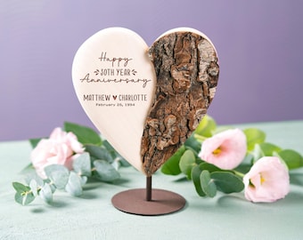 May include: A wooden heart-shaped plaque with a bark texture on one side and a smooth surface on the other. The plaque has the text "Happy 30th Year Anniversary Matthew ♥ Charlotte February 26, 1994" engraved on it. The plaque is on a metal stand.