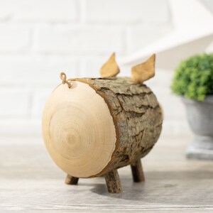 May include: A wooden pig figurine made from a tree trunk with a natural bark texture. The pig has a small tail made of twine and two small ears.