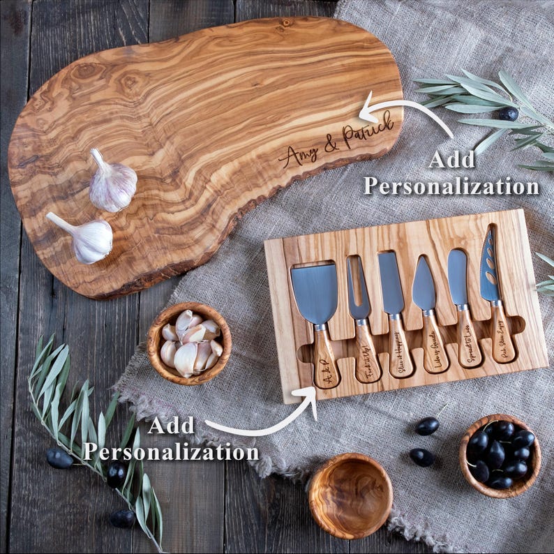 Op de afbeelding: Een houten kaasplank met een natuurlijke rand, gepersonaliseerd met de namen "Amy & Patrick". Inclusief een set kaasmesjes en kleine houten kommen met knoflook en olijven. De set is ontworpen voor personalisatie.