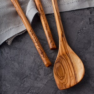 May include: Three wooden spoons with engraved sayings. The spoons are made of olive wood and have a natural wood grain. The sayings on the spoons are "You're my secret ingredient", "You're the recipe for success", and "You're my secret ingredient".