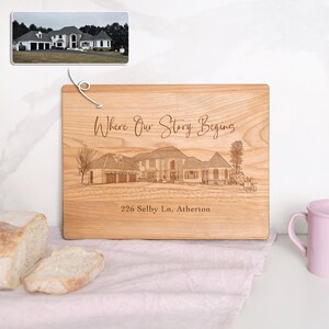 Puede incluir: Una tabla de cortar de madera con una imagen grabada con l&aacute;ser de una casa y el texto "Where Our Story Begins" y "226 Selby Ln, Atherton".