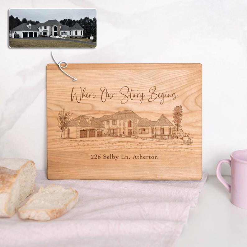 Puede incluir: Una tabla de cortar de madera con una imagen grabada con l&aacute;ser de una casa y el texto "Where Our Story Begins" y "226 Selby Ln, Atherton".