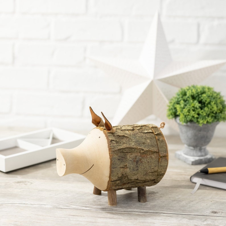 May include: A wooden pig figurine with a brown bark-like texture and a light brown snout. The pig has small brown ears and stands on four wooden legs.