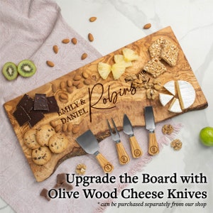 May include: Personalized olive wood serving board with the names "Emily & Daniel" and "Robbins" engraved on it. The board is filled with various snacks, including cheese, crackers, fruit, and nuts.  The board is also accompanied by a set of olive wood cheese knives.