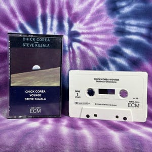 May include: A white cassette tape with the title "Chick Corea/Voyage" and the text "Mallorca/Diversions". The cassette tape is labeled "Side 1" and has a running time of 23:45. The cassette tape is from the ECM label and has the catalog number ECM 4-25013.