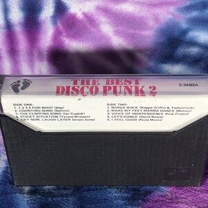 May include: A black cassette tape with the title "The Best Disco Punk 2" printed in red and white. The cassette tape has a white label with the track list for side one and side two. The cassette tape has a catalog number of S-3493A.
