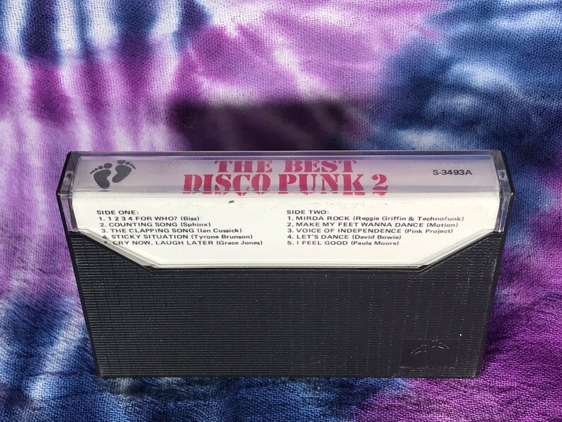 May include: A black cassette tape with the title "The Best Disco Punk 2" printed in red and white. The cassette tape has a white label with the track list for side one and side two. The cassette tape has a catalog number of S-3493A.