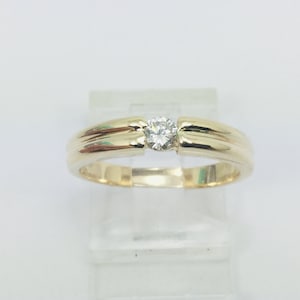 Puede incluir: Un anillo de banda de oro con un solo diamante redondo en el centro.