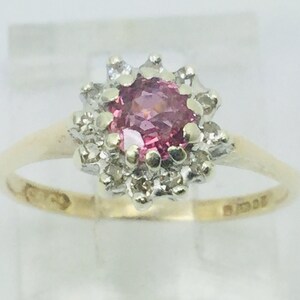 May include: A gold ring with a pink gemstone surrounded by a halo of smaller white gemstones.