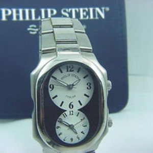 May include: A silver Philip Stein watch with a black face and two dials. The watch has a unique oval shape and a silver metal strap.