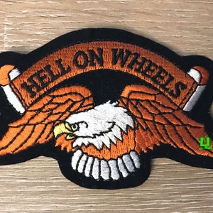 May include: An orange and white embroidered patch featuring an eagle design and the text "Hell on Wheels".