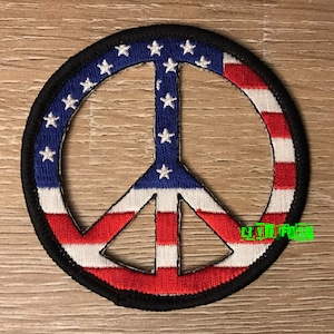 May include: A peace sign patch with the American flag design. The patch is red, white, and blue with a black border.