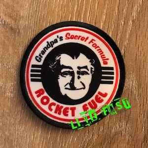 May include: A black and white circular patch with red and white trim. The patch features a cartoon image of a man's face with the text "Grandpa's Secret Formula Rocket Fuel" around the image.