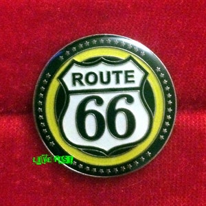 Könnte beinhalten: Eine silberne Metallstifte mit einem schwarz-weißen Route 66-Schild mit gelbem Rand und einem Sternenkranz außen herum.