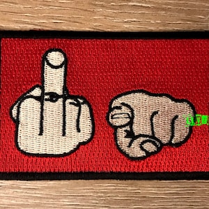 Könnte beinhalten: Roter gestickter Aufnäher mit zwei weißen Mittelfingern, einer zeigt nach oben und der andere nach vorne.