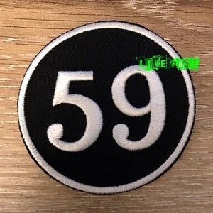 May include: A circular embroidered patch featuring a black background with a white border and the large white number 59 centered in the middle. The text LIVE FAST is visible in bright green letters in the upper right quadrant of the patch.